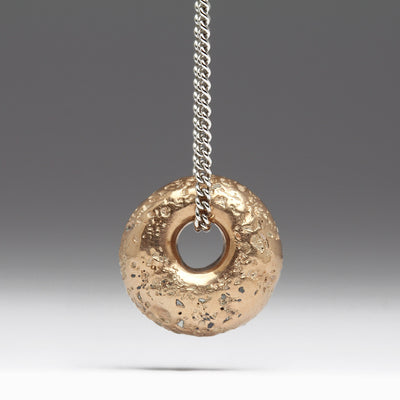 A 9ct gold sandcast blush gold drop pendant suspended on an 18-inch white gold curb chain against a grey background.